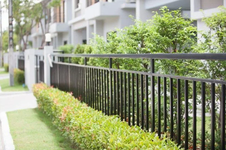 A trusted Fencing Contractor in Galt CA installing a modern black metal fence alongside a manicured green hedge.