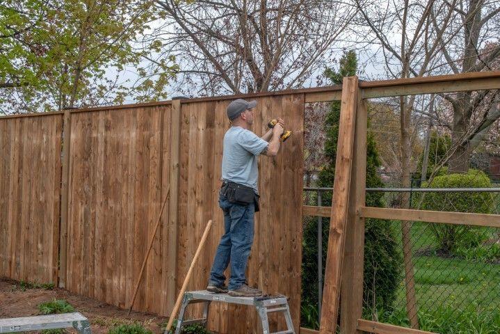 A Fencing Contractor in Galt CA standing on a step stool while installing tall wooden fence panels.