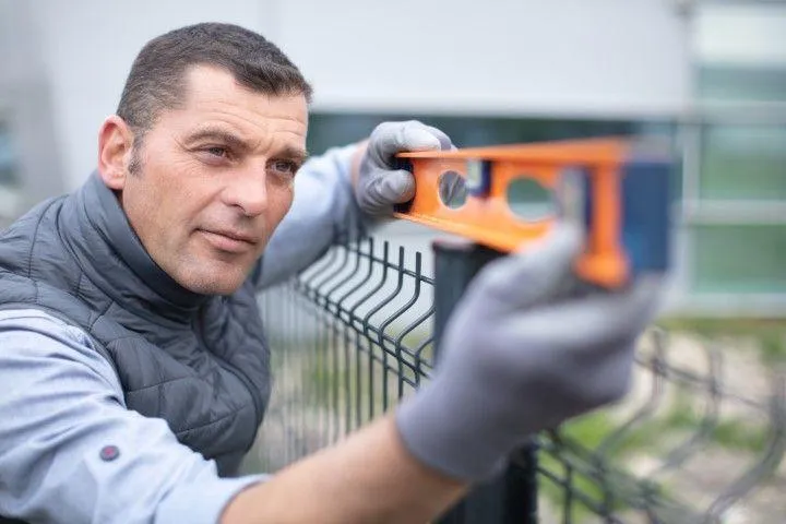 A professional Fencing Contractor in Galt CA using a level tool to align a wire mesh fence post.