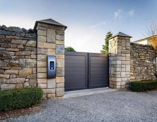 Professional Fencing Contractor in Galt CA installing a modern dark metal driveway gate between stacked stone pillars.