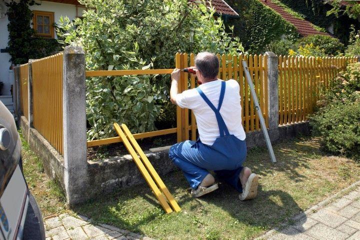 Expert Fencing Contractor in Galt CA repairing a yellow wooden picket fence mounted on a low concrete retaining wall.