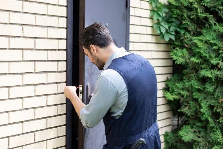 A man in work overalls installing a door in a beige brick wall, an example of Custom Carpentry Creations in Clovis.