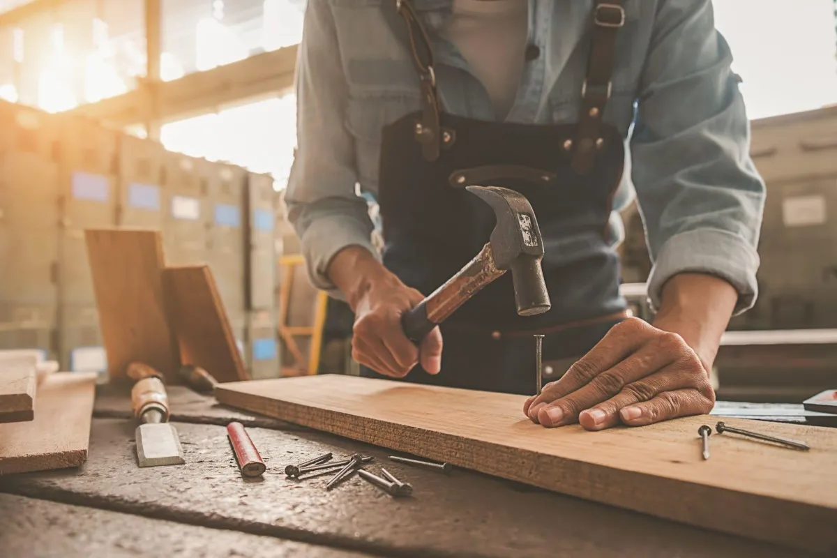 Close-up of a carpenter in an apron hammering a nail into wood, representing Custom Carpentry Creations in Clovis.