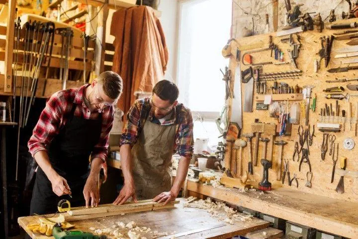 Two carpenters collaborate at a workbench with a detailed pegboard wall, showcasing Custom Carpentry Creations in Clovis.
