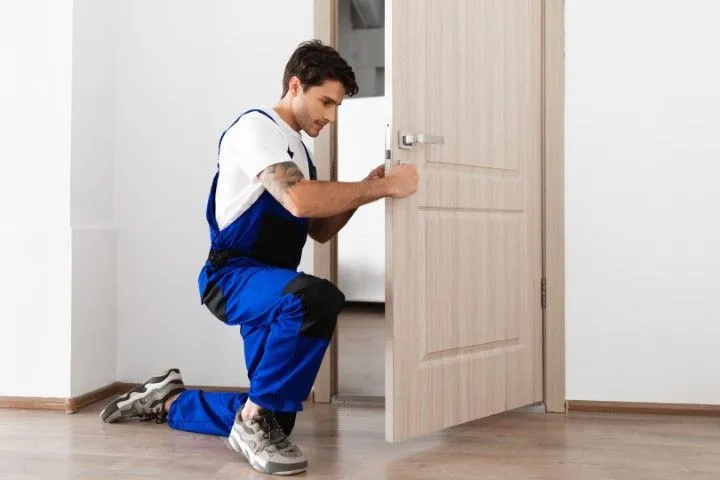 A skilled professional installer from Custom Carpentry Creations in Clovis kneels to fit a new wooden interior door and handle.
