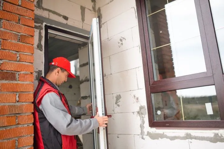 A specialist in a red vest and cap from Custom Carpentry Creations in Clovis installs a white exterior door in a block wall home.