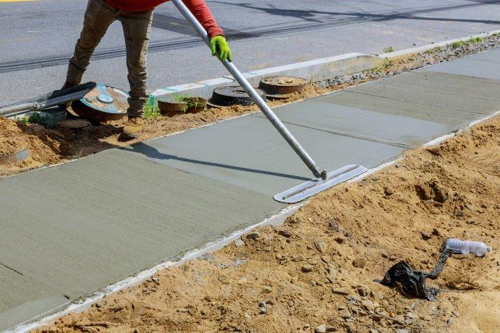 A skilled concrete contractor in Dania Beach FL smooths a freshly poured sidewalk with a fresno trowel.