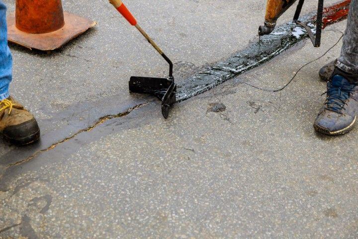 Close-up of a concrete contractor in Dania Beach FL repairing a crack in a textured asphalt driveway.