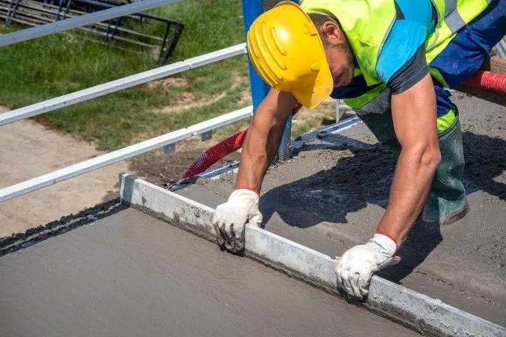 A concrete contractor in Dania Beach FL uses a screed to level a fresh slab on a sunny construction site.