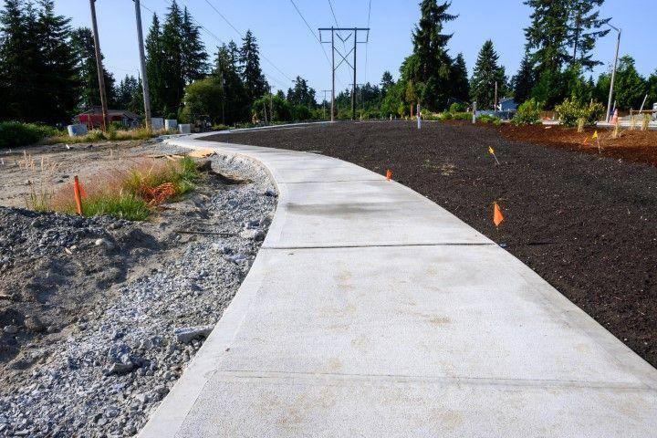 A winding concrete sidewalk built by a concrete contractor in Dania Beach FL alongside freshly landscaped soil.