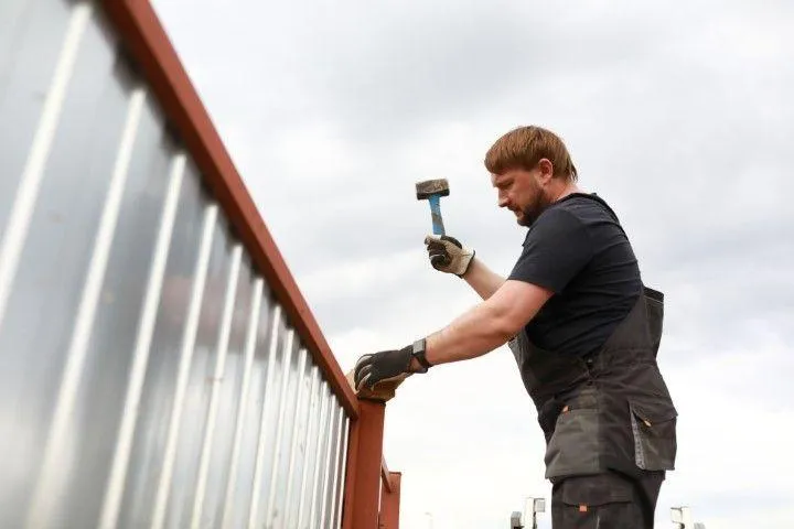 A professional Fencing Contractor in Exeter PA hammers a post, building a sturdy metal and wood fence on a job site.