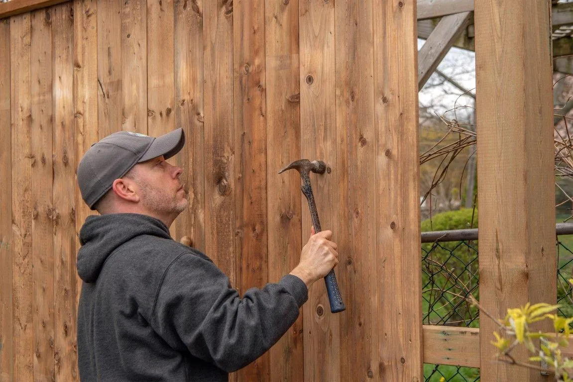 A technician hammering a wooden panel, provided by Paso Robles Fencing Pros, in Paso de Robles CA.