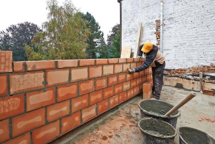 Clarington Masonry Craftsmen in Clarington ON building a new brick wall outdoors with mortar buckets.