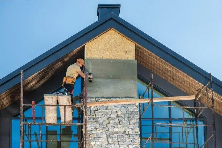 A skilled mason working on a custom stone chimney and roofline, representing San Gabriel Masonry in San Gabriel CA.