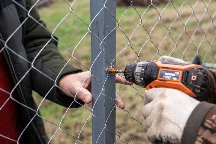 Sandusky Fencing Creations in Sandusky OH repairing a chain link fence with a drill.