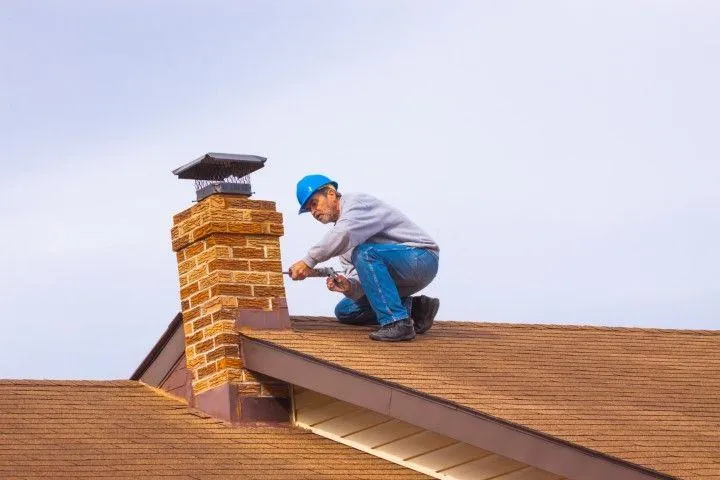 Clarington Masonry Craftsmen in Clarington ON repairing a brick chimney on a shingled roof.