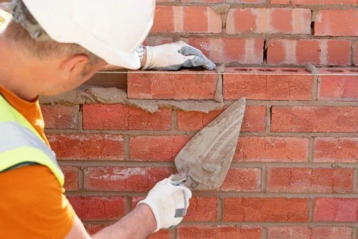 Clarington Masonry Craftsmen in Clarington ON smoothing wet mortar between red bricks with a hand trowel.