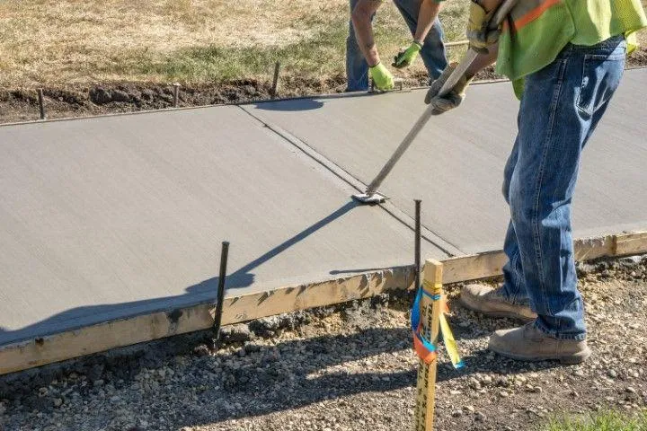 A skilled concrete contractor in Dania Beach FL smooths a freshly poured sidewalk with a fresno trowel.