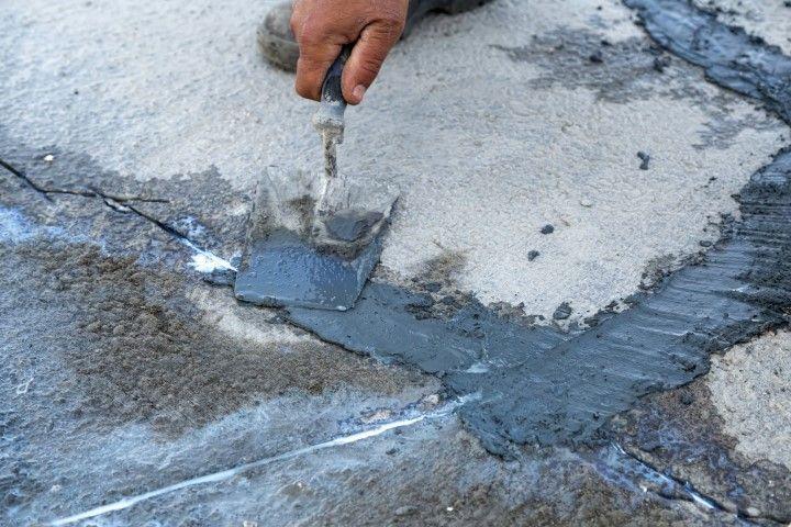 Close-up of a concrete contractor in Dania Beach FL repairing a crack in a textured asphalt driveway.