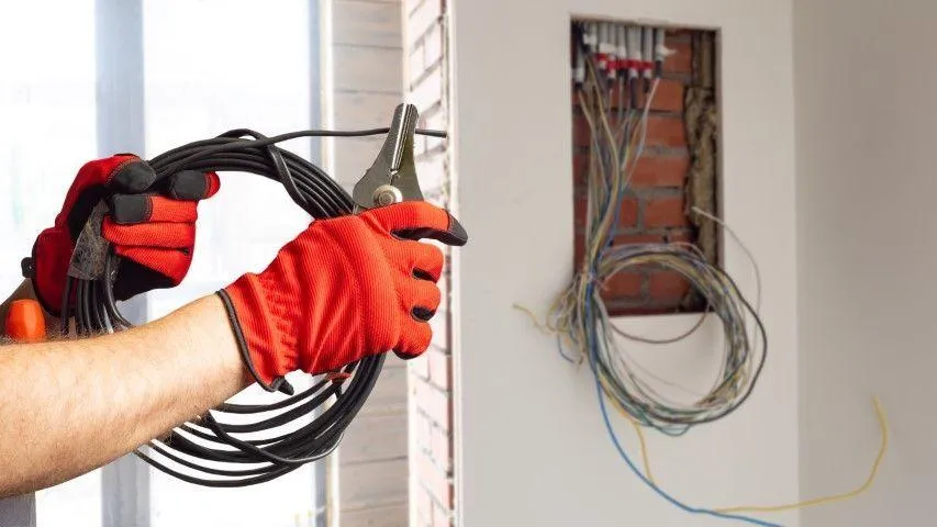 Worker in red gloves holding a coil of black wire for Falls Electric Services Company in Falls PA.