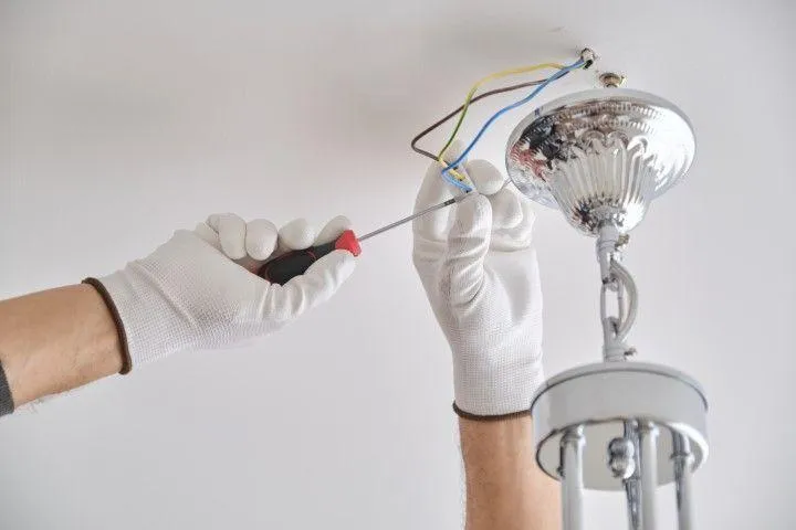 Grandview Electrical Pro in Grandview MO installing a shiny chrome chandelier light fixture on a ceiling.