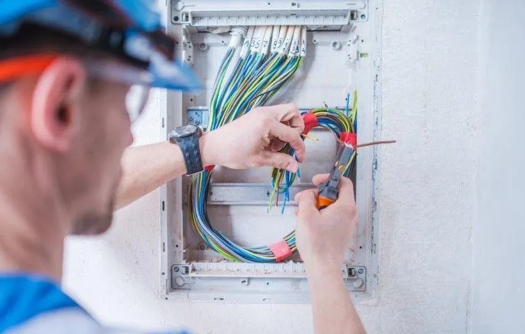 Grandview Electrical Pro in Grandview MO stripping wires inside a wall-mounted electrical panel box.