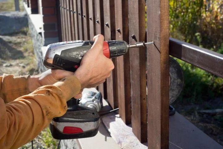 Sandusky Fencing Creations in Sandusky OH using a power drill to fix wooden panels onto a fence.