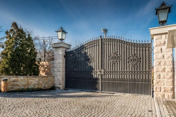 Sandusky Fencing Creations in Sandusky OH showcasing a grand ornate iron driveway gate between stone pillars.