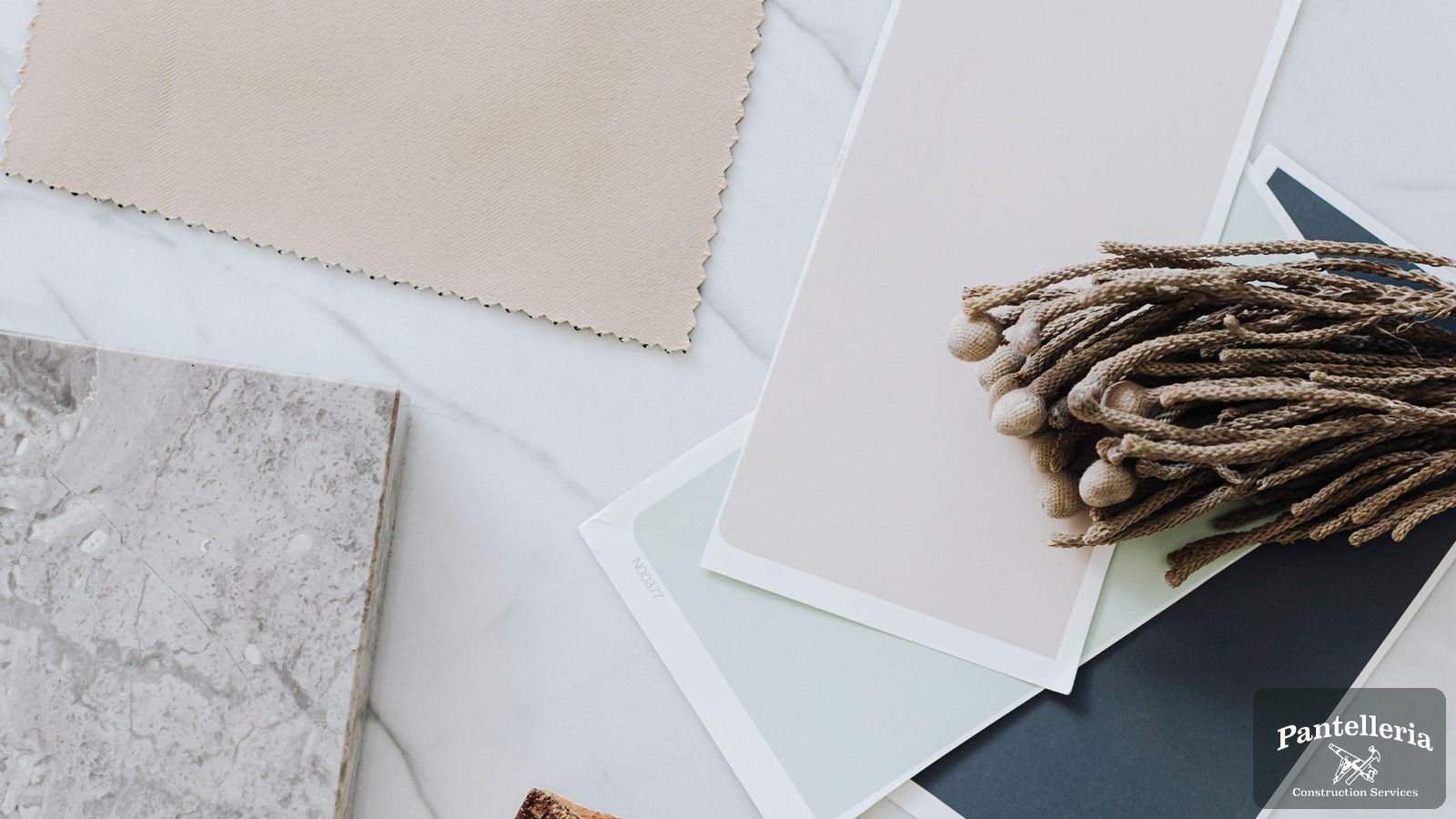 Flat lay of remodel selections on a marble counter: a stone countertop sample, fabric swatch, paint chips and a live-edge wood sample