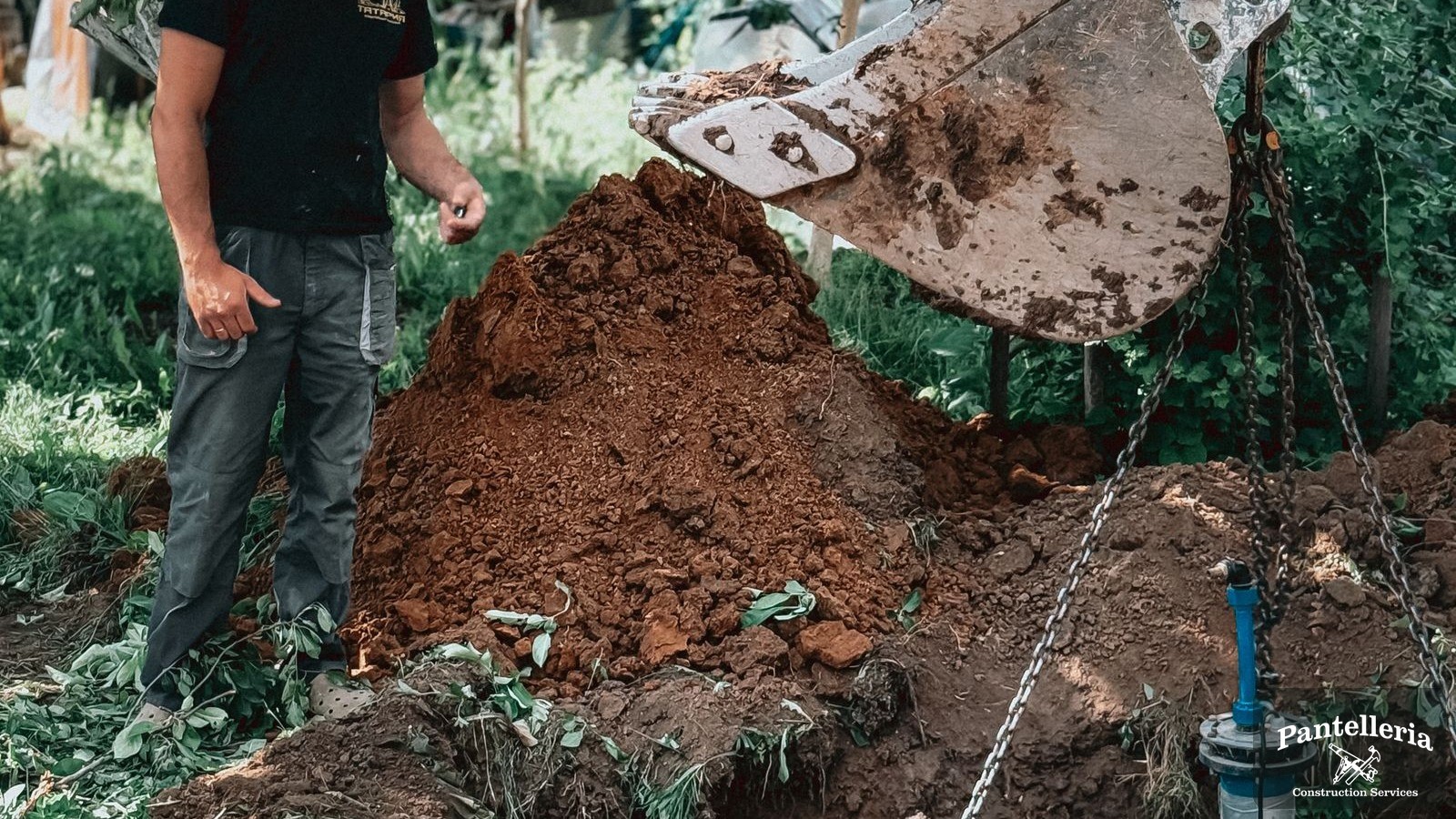 Excavator lowering a concrete well ring into a dug pit on a rural building site