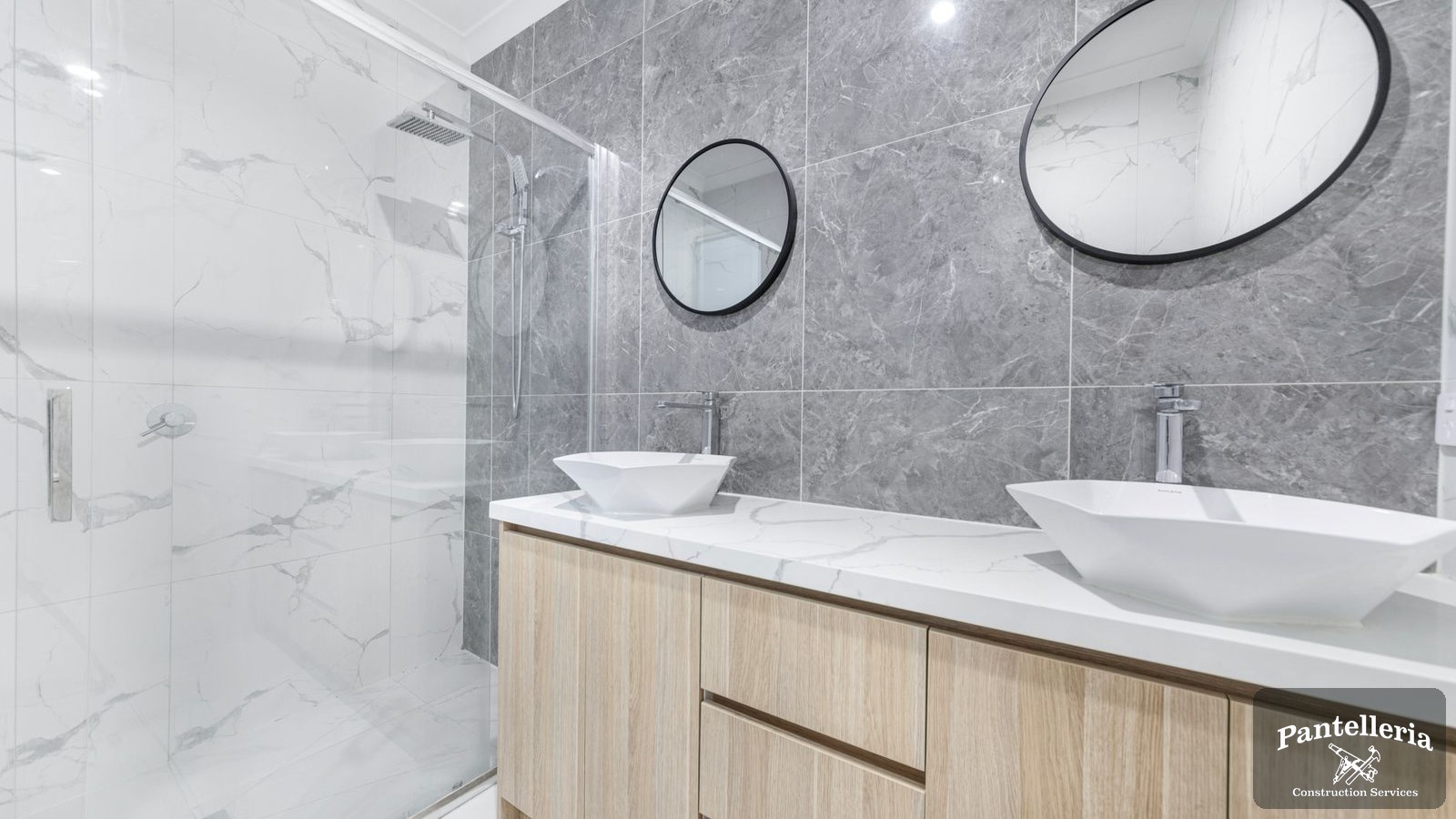 Renovated bathroom with marble tile, double vanity and a glass shower