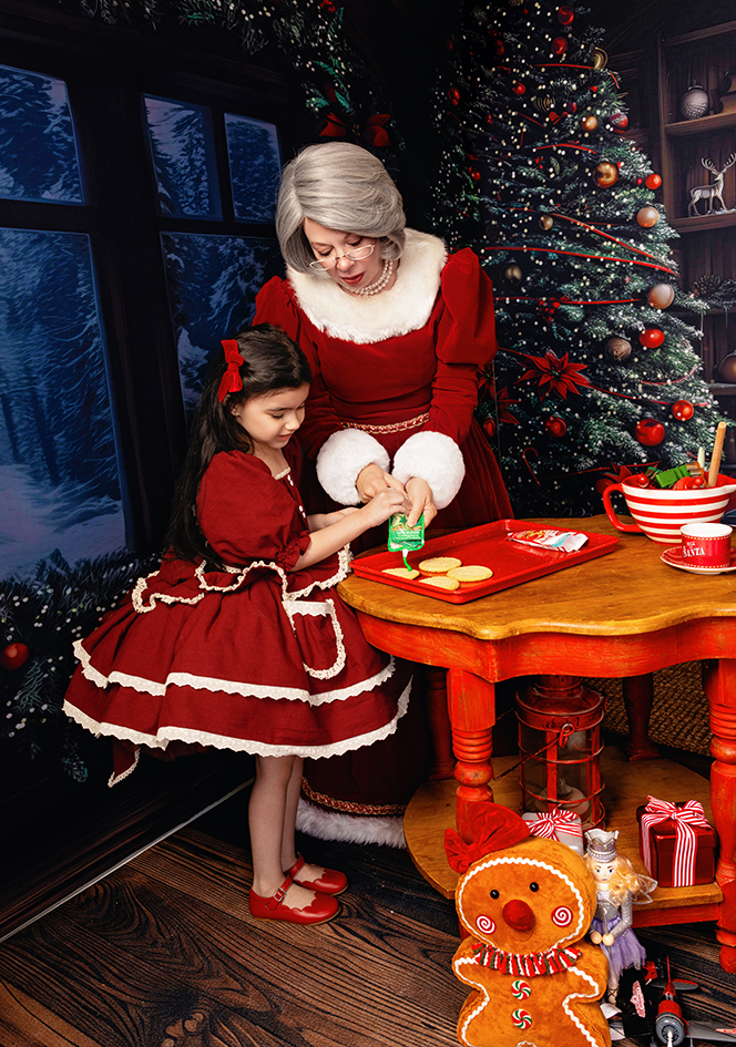 Mrs. Claus and a girl decorate Christmas cookies together.
