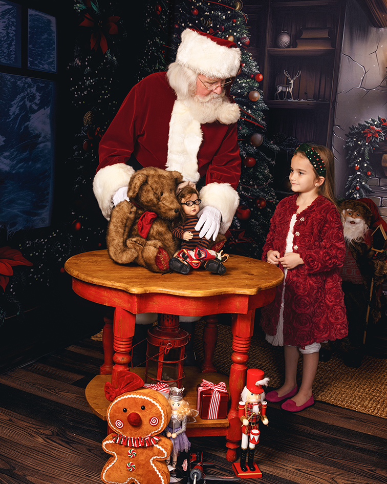 Santa and a girl discover toys at a table in Santa's workshop.
