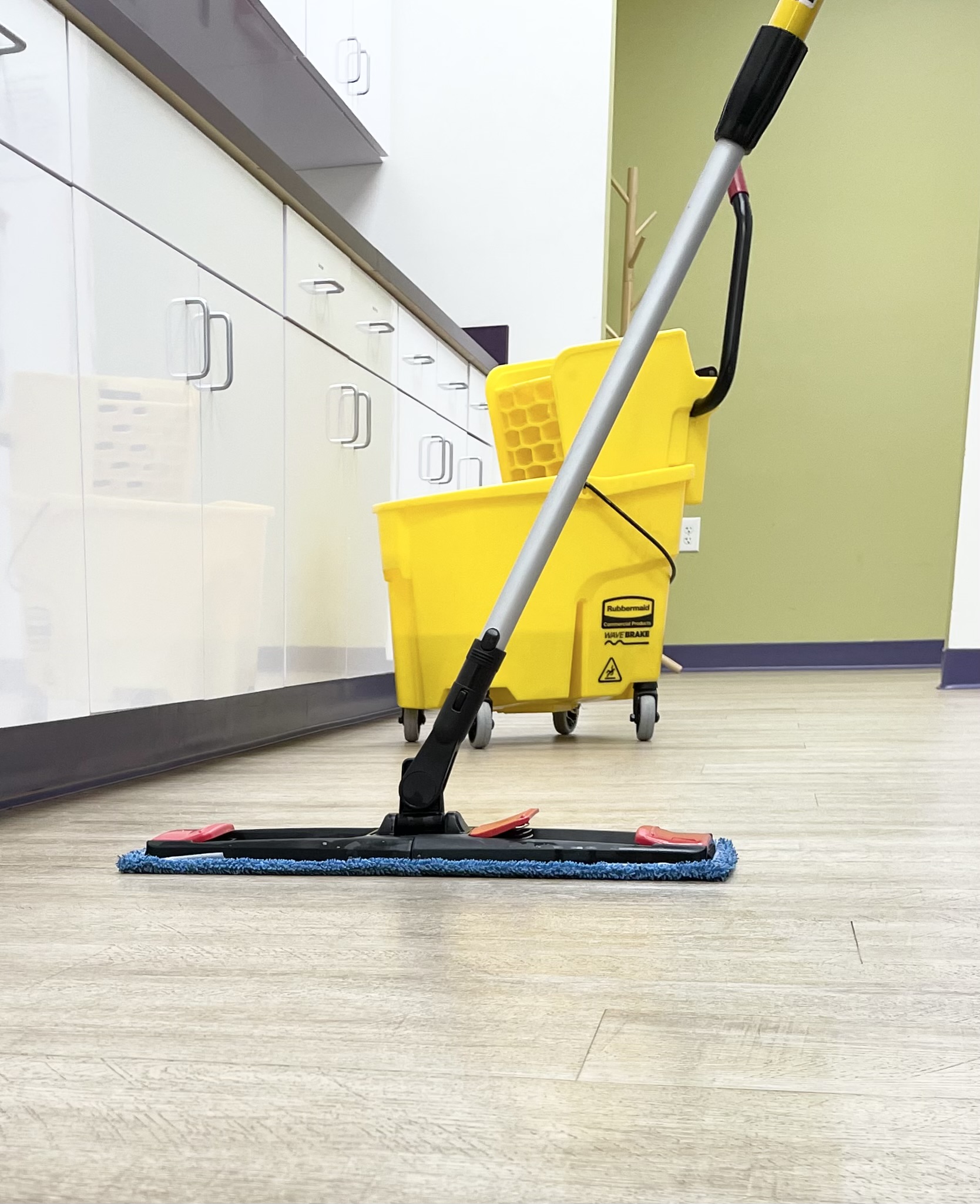 A microfiber flat mop cleaning the floor of a medical office with a yellow mop bucket in the background.