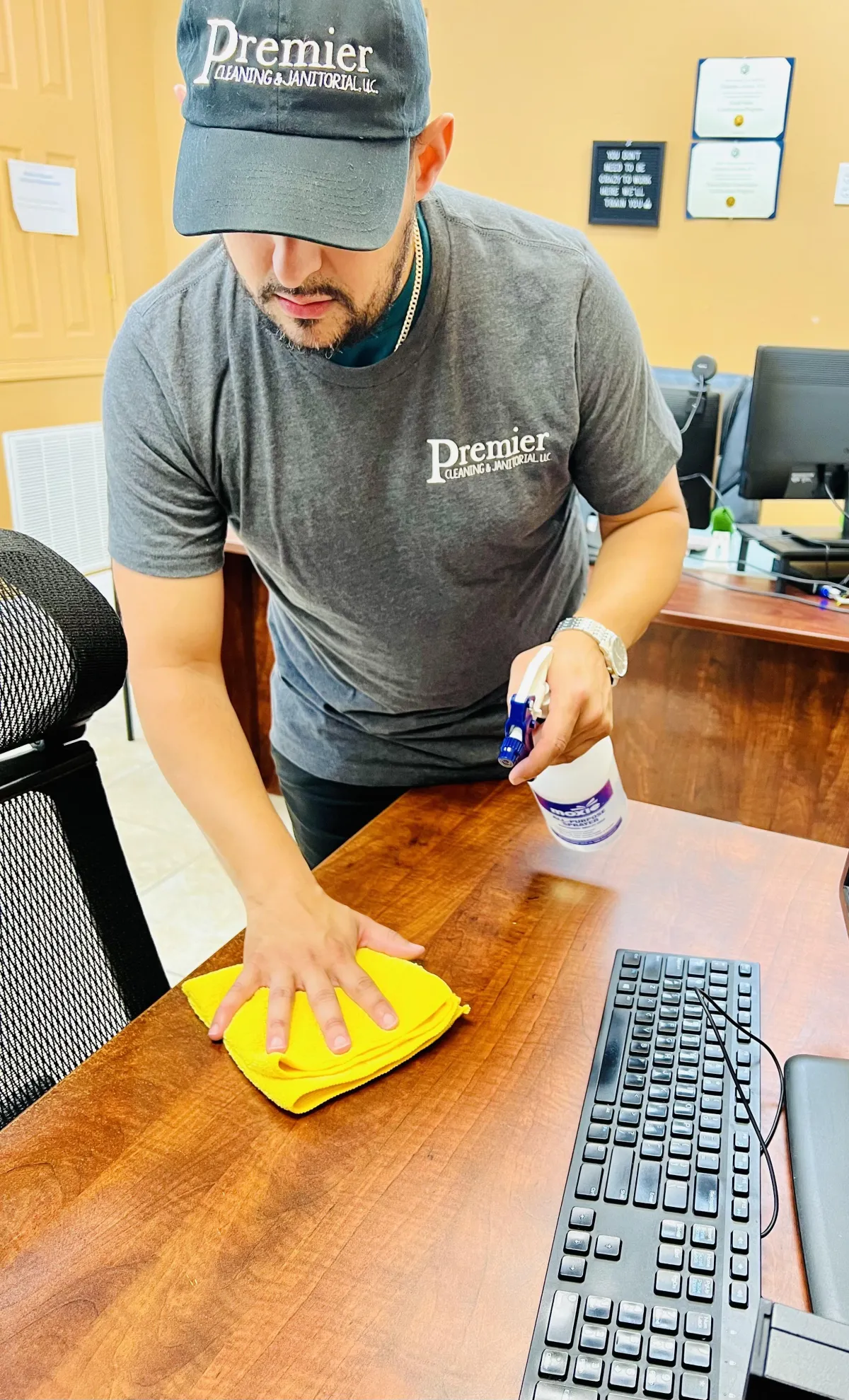 Premier Cleaning Crew Member wiping down desk with yellow microfiber towel.