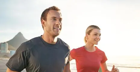 Active young man and woman jogging along a scenic path near the water, representing vitality, fitness, and outdoor lifestyle.