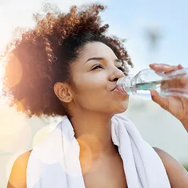 Young woman hydrating after a workout, smiling with a towel over her shoulders, representing healthy habits and self-care.