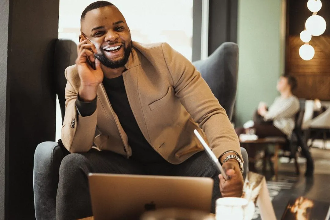 Smiling business owner sitting in a modern café, speaking on the phone with a laptop open in front of him, looking confident and relaxed — representing the freedom and clarity that comes from understanding your business finances.