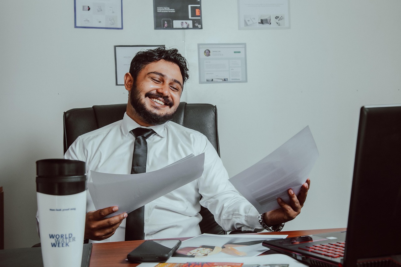 Smiling business owner sitting in a modern café, speaking on the phone with a laptop open in front of him, looking confident and relaxed — representing the freedom and clarity that comes from understanding your business finances.