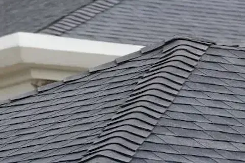 Close-up of buckled asphalt shingles showing moisture damage needing professional roof repair