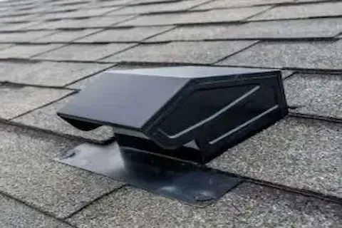 Black attic roof vent installed flush on asphalt shingles for improved home ventilation