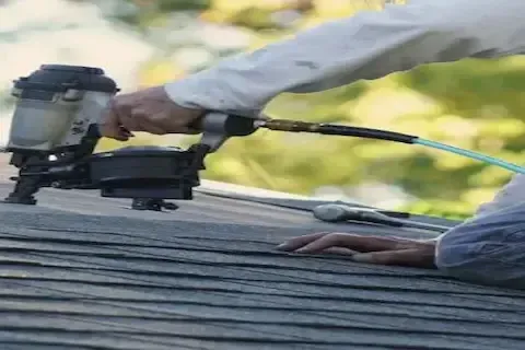 Roofer using pneumatic nail gun to fasten shingles during roof patching work