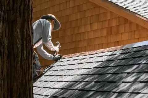 Roofer hand-nailing shingles along the slope during residential roof repair service