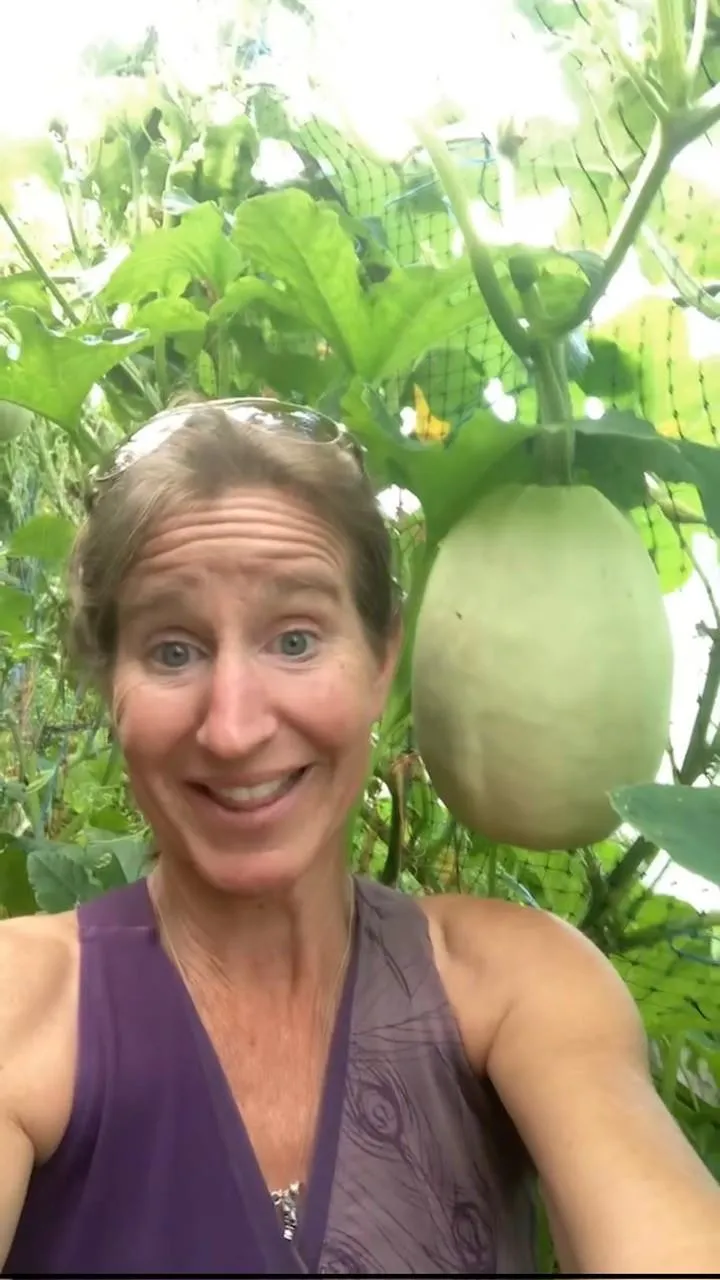 Founder, Erin Saunders smiling next to a large spaghetti squash hanging, almost the size of her head.