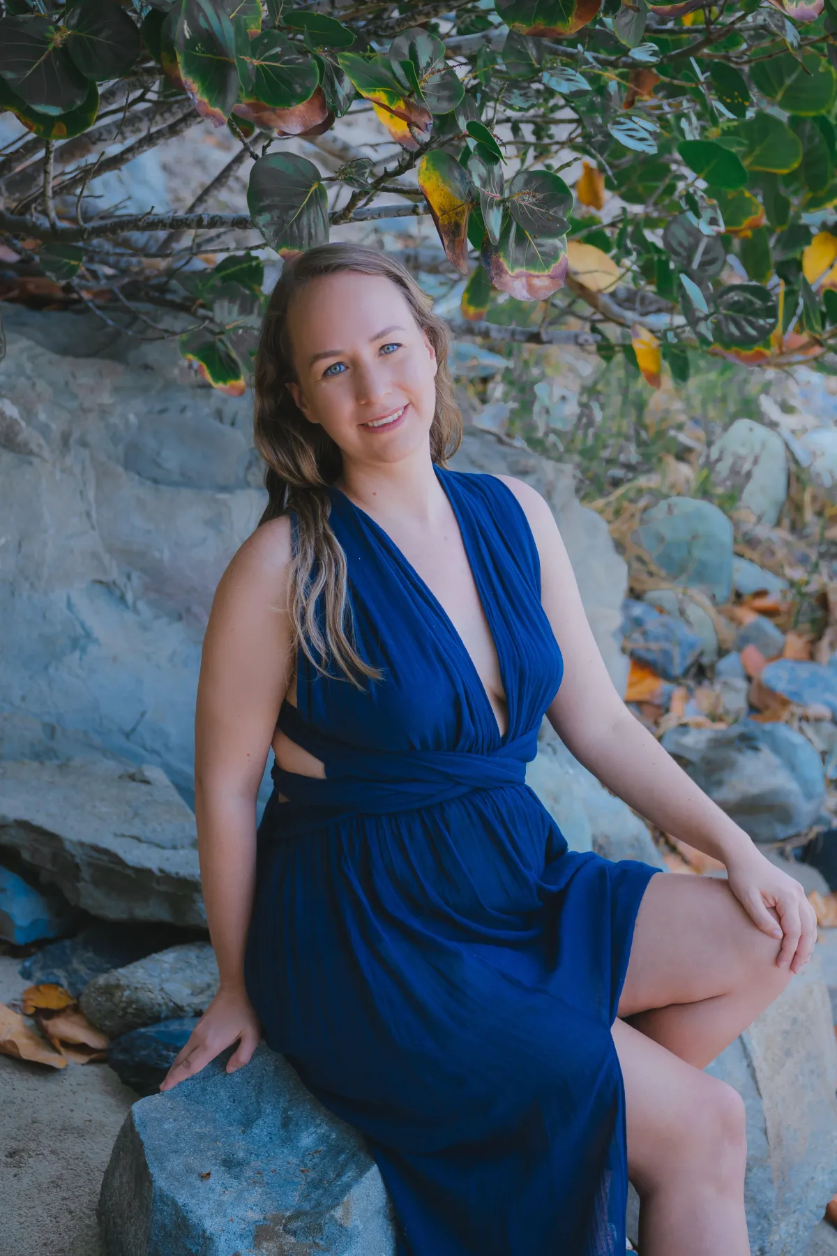 A woman in a blue dress sitting on a rock, enjoying the serene surroundings.