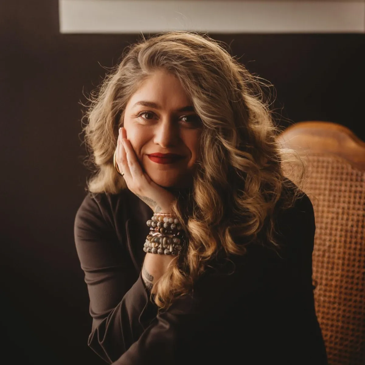 A woman with long curly hair sitting on a chair.