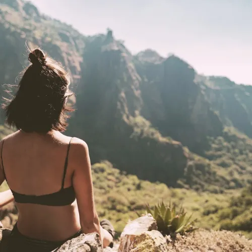 A woman sitting on a rock, gazing at a majestic mountain landscape.