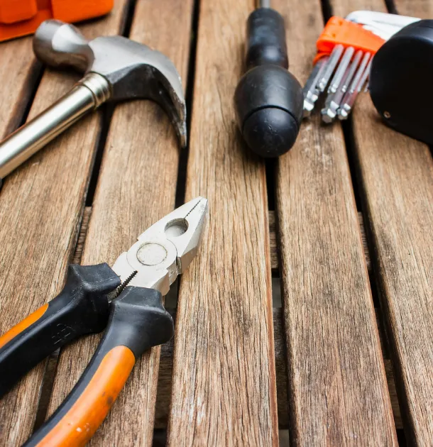 Home improvement tools including a hammer, pliers, and screws on a wooden surface.