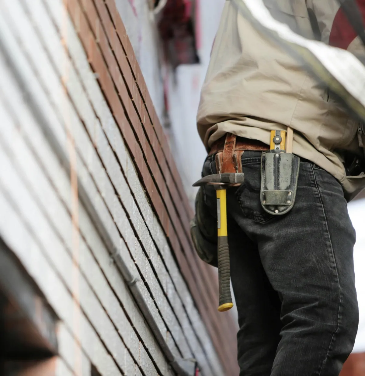 Construction worker with a hammer and tool belt standing next to a house under renovation.