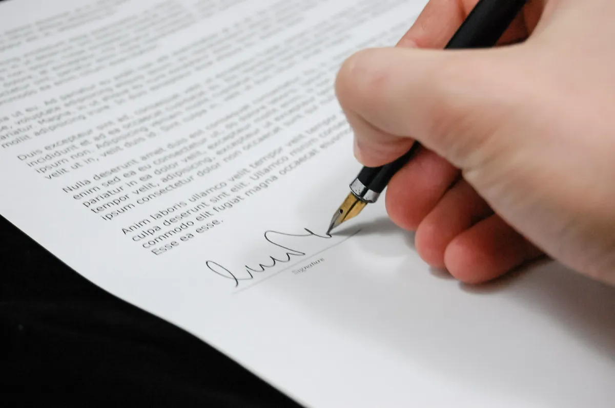 Person signing an escrow agreement for a real estate purchase in Mexico, with contract documents and a pen on a desk during the property closing process. Dream Baja Realty